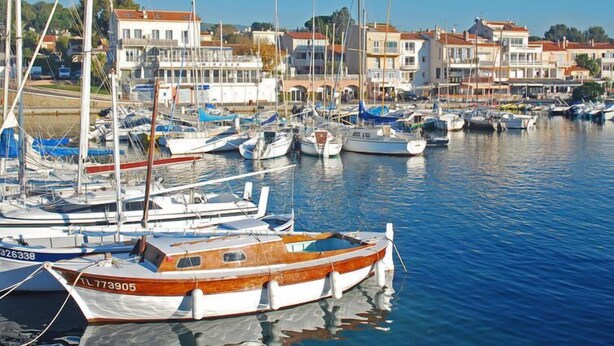 Un port de plaisance où sont amarrés différents types de bateaux, entouré de bâtiments résidentiels.