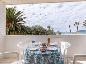 A table set for two with a patterned tablecloth, white chairs, and a view of the sea and palm trees.