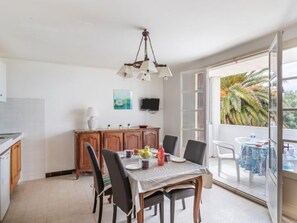 A dining area with a table set for four, a wooden cabinet, a television on the wall, and a view of palm trees through a large window.