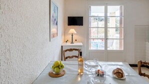 Un coin repas avec une table dressée pour deux personnes, une bouteille de vin, un saladier de fruits et une miche de pain.