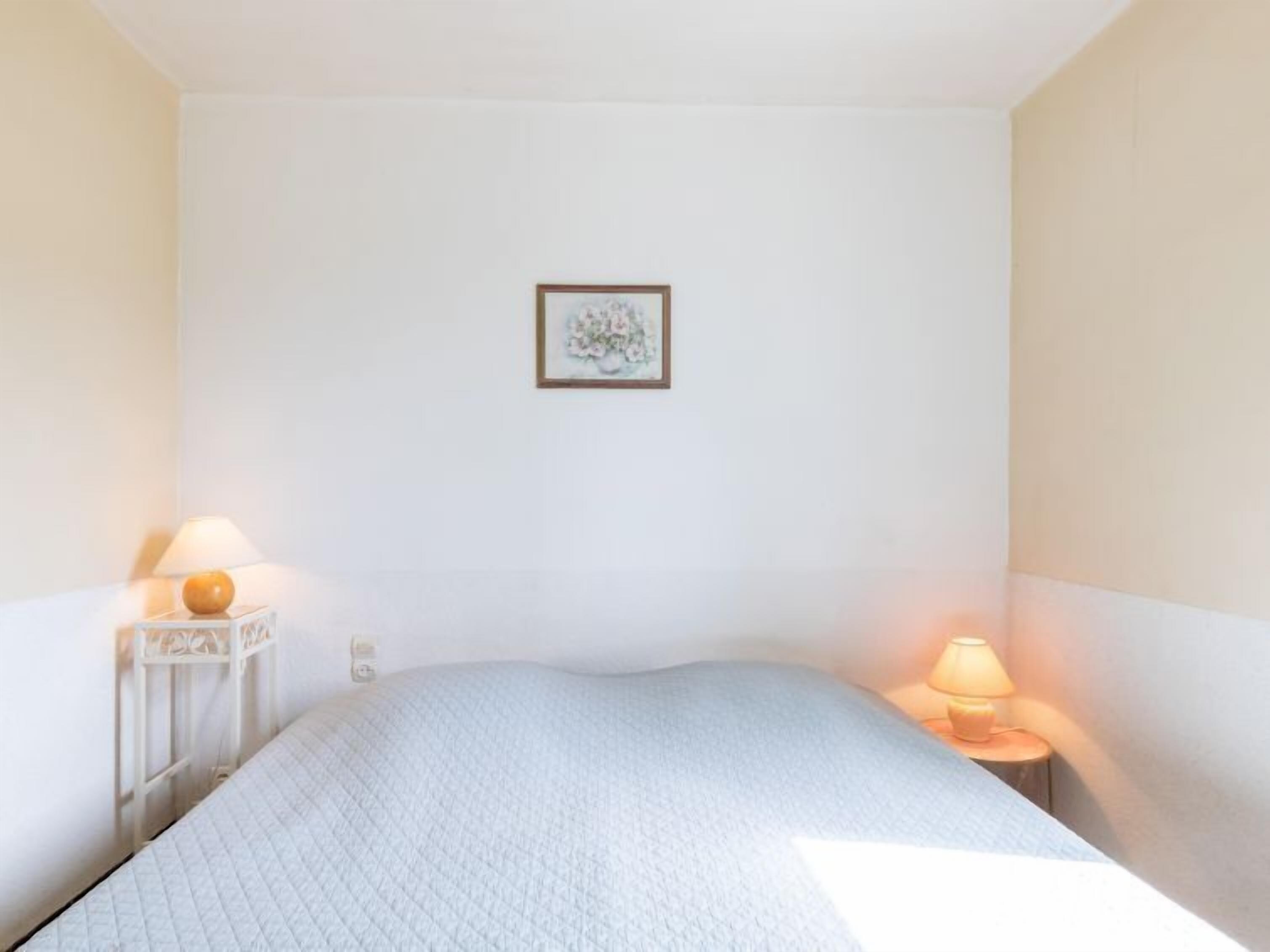 A bedroom with a single bed, two bedside tables with lamps, and a framed picture on the wall.