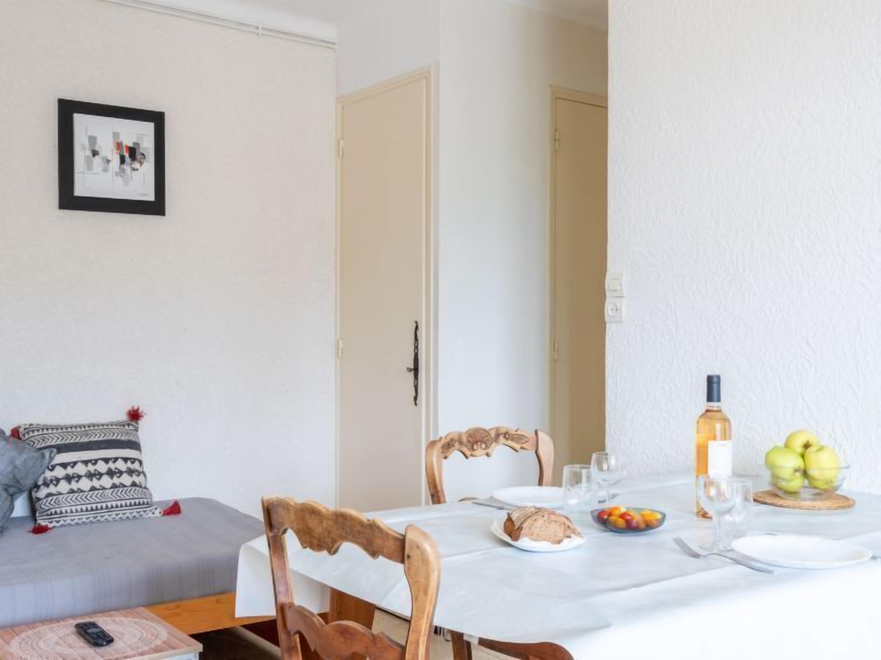 A dining area with a table set for two, a sofa with patterned cushions, and a framed picture on the wall.