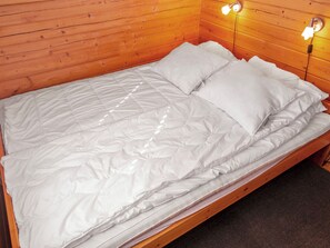 Una cama individual con colchón y almohadas blancos en una habitación con paredes de madera y dos lámparas de noche.