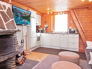 Interior acogedor de una cabaña con chimenea de piedra, cocina con armarios blancos y un ventanal grande.