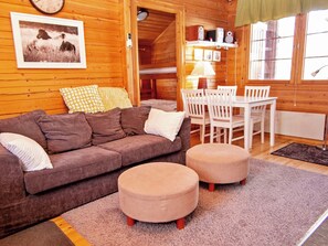 A cozy cabin interior with a brown sofa, two ottomans, a dining table with chairs, a lamp, and a clock on the wall. - Lomasyväri 810 by Interhome (Nilsiä)