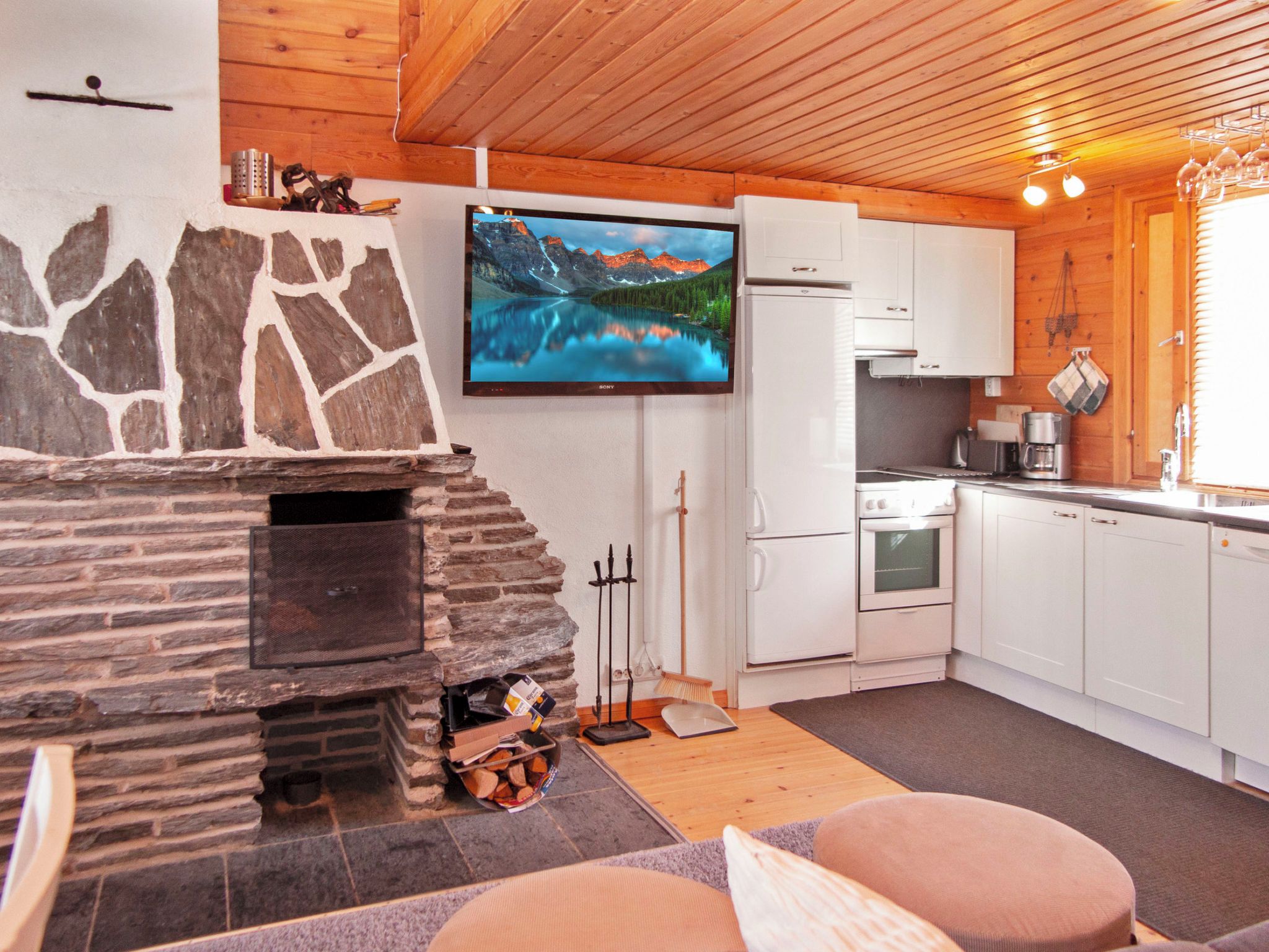 Una cocina acogedora con chimenea de piedra, televisor y electrodomésticos modernos.