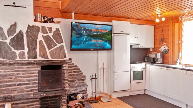 Eine moderne Küche mit weißen Schränken, einem Kamin aus Stein, einem Flachbildfernseher und einer Holzbalkendecke.