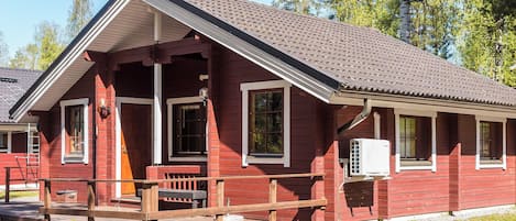 A red wooden building with a pitched roof, a porch, and a gravel driveway.