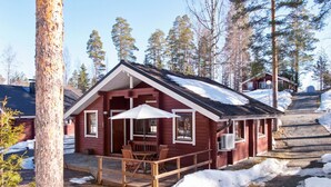 Eine Hütte mit einer Holzterrasse, Sitzgelegenheiten im Freien und einem mit Schnee bedeckten Gelände.