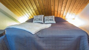 Un lit avec deux oreillers, chacun portant l’inscription « Il n’y a pas d’endroit comme chez soi ». Le lit est recouvert d’une courtepointe bleue et d’un plaid blanc.