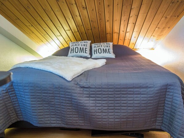 A bed with two pillows, each with the text "There is no place like HOME." The bed has a blue quilt and a white throw blanket. - Tahkon klubitie 4 a by Interhome (Nilsiä)