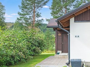 Ein Wohngebäude mit einer braunen Tür, der Hausnummer '4A' an der Wand und einem gepflegten Garten mit einer Hecke und einem Rasen.