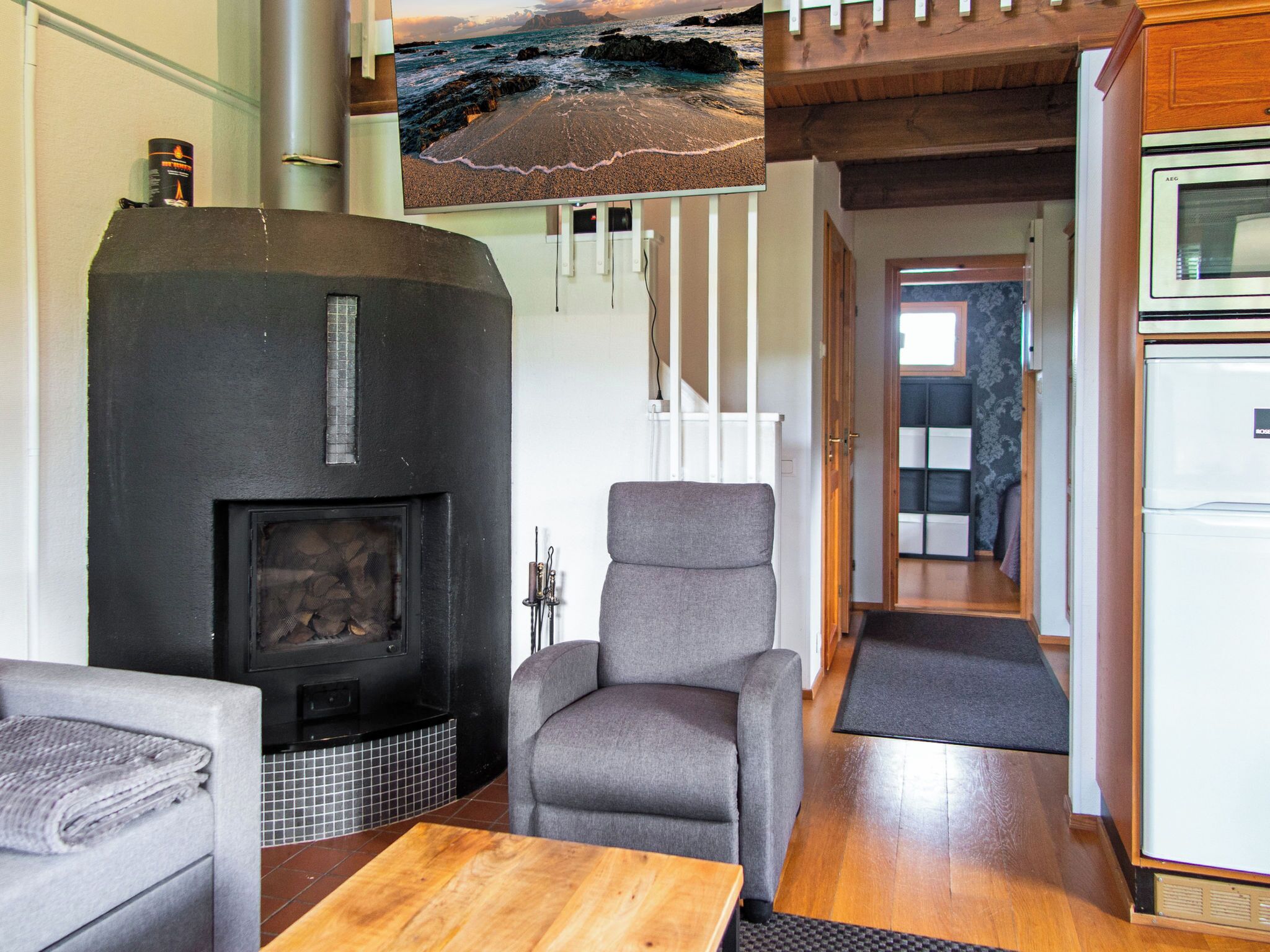 A living room with a fireplace, a sofa, a wooden table, and a view of the sea through a window.