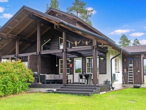 Una cabaña de madera con un porche, mobiliario exterior y un espacio cubierto.