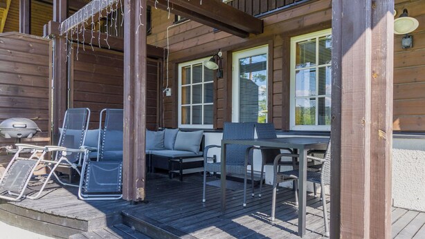 Une terrasse en bois avec un espace salon extérieur comprenant des chaises et un canapé, ainsi qu’un barbecue.