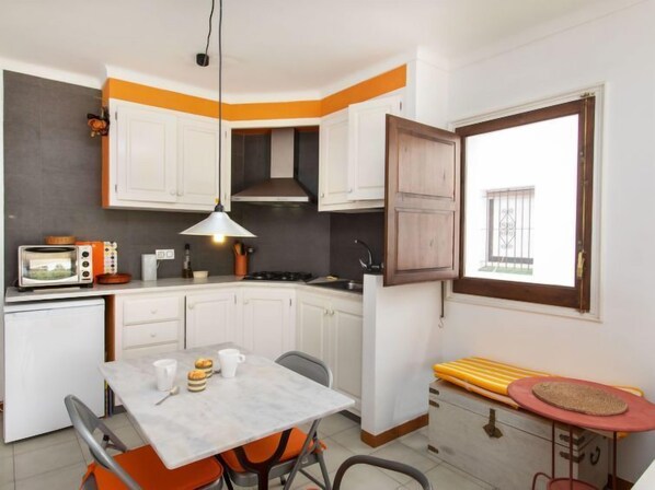 A compact kitchen with white cabinets, a microwave, a gas stove, and a dining table with chairs. - Edifici Port del Rei by Interhome (L'Escala)