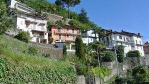 A hillside residential area with multi-story buildings, some with balconies, surrounded by greenery and trees. - Casa Lago Azzurro Atelier relaxation puur for vacation & time out (Cannobio)