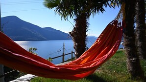 A hammock tied between two palm trees overlooking a lake with mountains in the background. - Casa Lago Azzurro Atelier relaxation puur for vacation & time out (Cannobio)