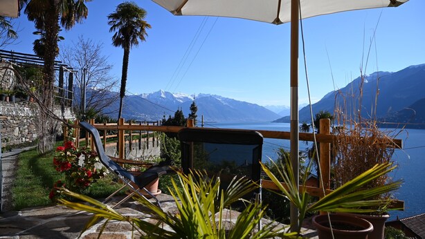 A terrace with a view of a lake and mountains, featuring a wooden fence, potted plants, and a chair. - Casa Lago Azzurro Atelier relaxation puur for vacation & time out (Cannobio)