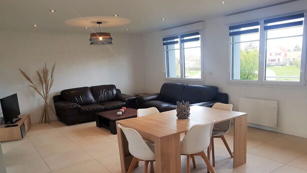 A modern living room with a black leather sofa, a wooden dining table with white chairs, a television on a wooden stand, and a decorative vase. - Condette, ideally located house! (Condette)