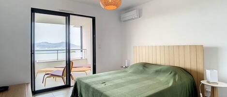 A bedroom with a bed, a small table, a chair, and a balcony with a view.