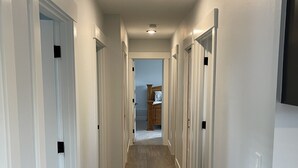 A hallway with white walls, wooden flooring, and multiple doors. - Beautiful relaxing home 4BR/3BA near Light Rail (Seattle)