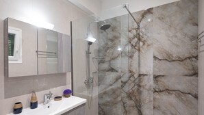 A modern bathroom with a glass-enclosed shower, a white sink, and marble walls. - Villa Olga by Corfuescapes (Corfu)