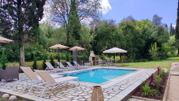A swimming pool with lounge chairs and umbrellas, surrounded by greenery and a barbecue area. - Villa Olga by Corfuescapes (Corfu)