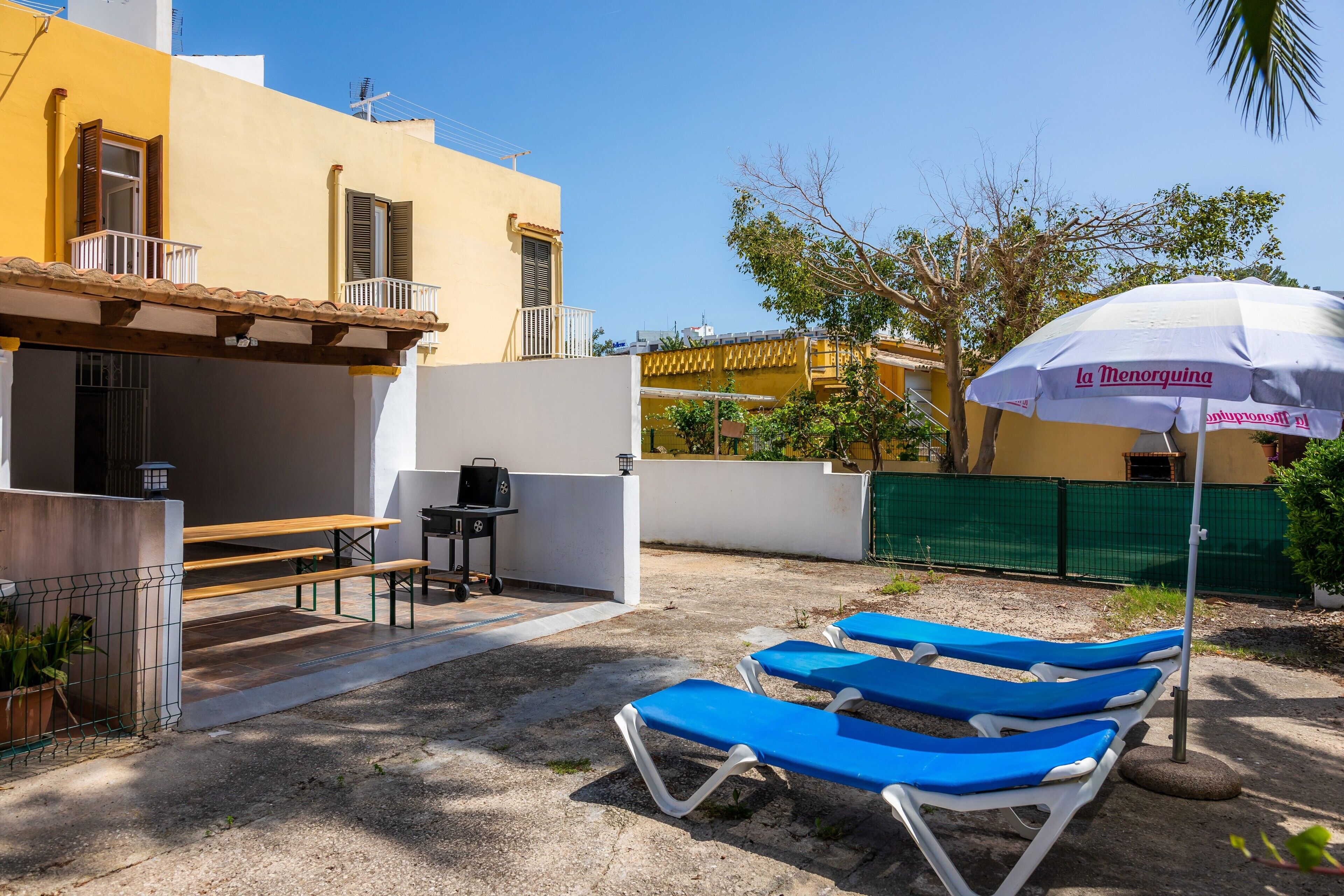 Eine Terrasse mit blauen Lounge-Stühlen, einem Grill und einem Tisch.