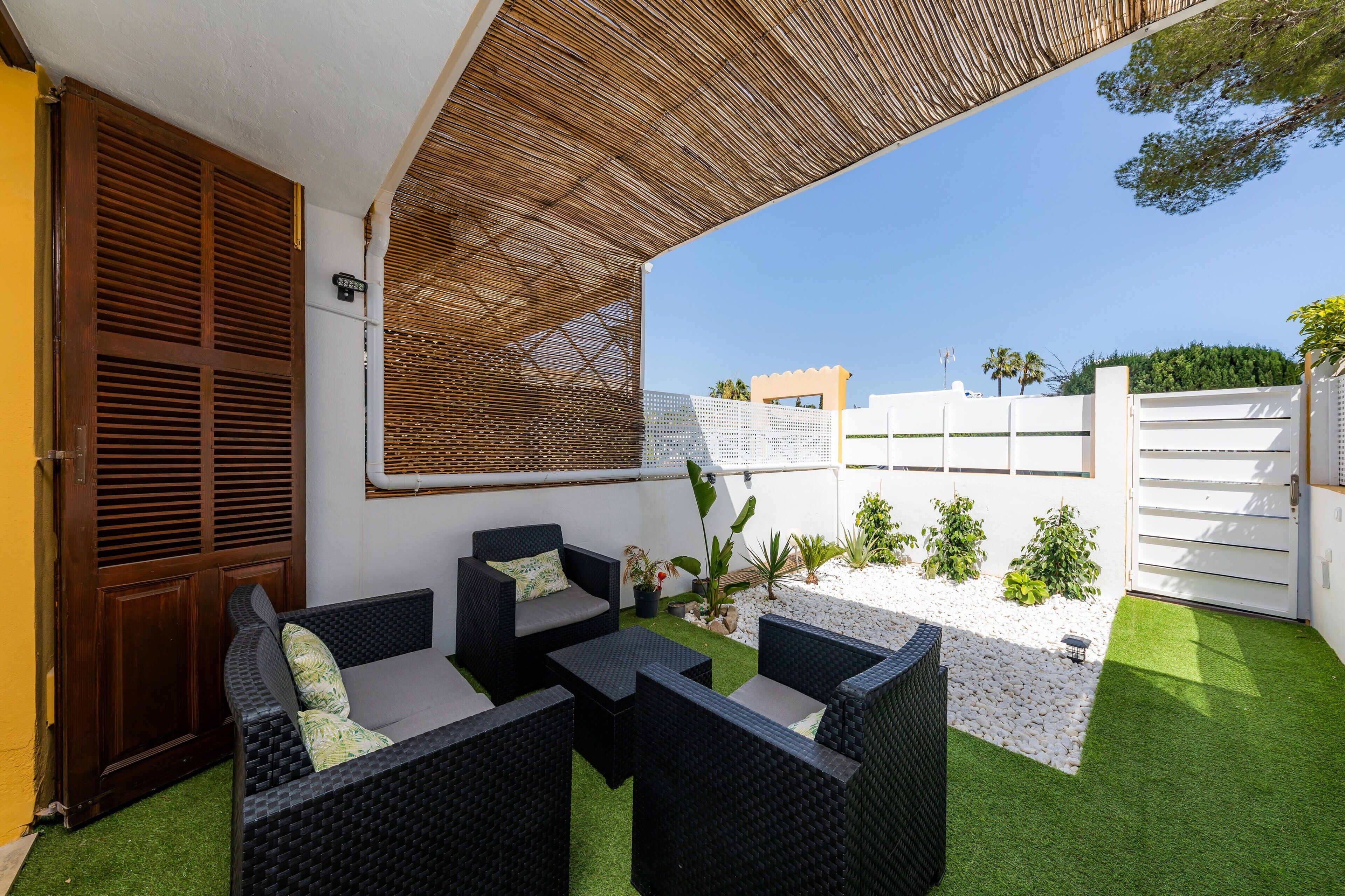 Eine Terrasse mit Korbmöbeln, einer Holztür und einem weißen Zaun.