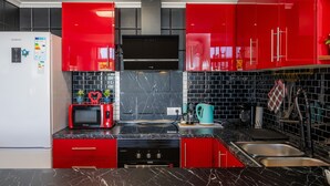 A kitchen with red cabinets, a black tiled backsplash, a microwave, a stove, and a sink.