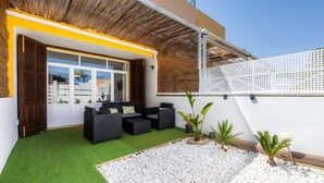 A modern outdoor seating area with artificial grass, white pebbles, and black furniture.