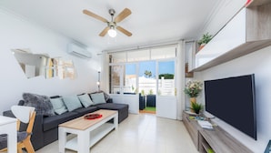 A modern living room with a sofa, coffee table, TV, ceiling fan, and large windows.