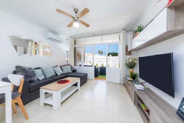 Un salon moderne comprenant un canapé, une table basse, un téléviseur, un ventilateur de plafond et de grandes fenêtres.