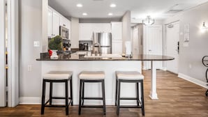 A modern kitchen with white cabinets, a stainless steel refrigerator, a granite countertop, and three bar stools. - Heritage Crossing Magic | 3BR, 2 Bath Cozy Condo w/ Golf Course Views and Themed Room Near Disney (Kissimmee)