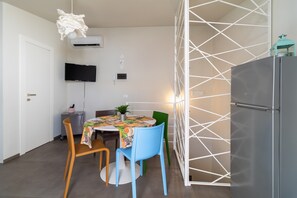 Una cocina compacta con una mesa de comedor, sillas, un refrigerador, un televisor y un separador blanco.