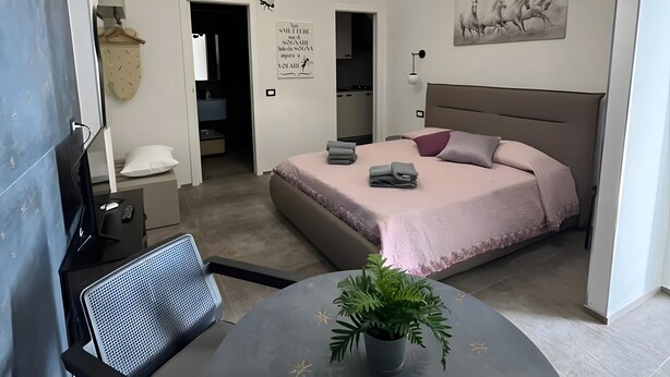 A modern bedroom with a bed, bedside tables, a desk, a chair, a round table with a plant, and two pendant lights.