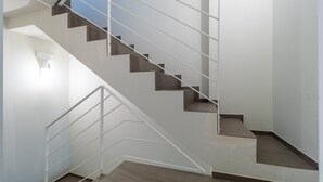 A staircase with a metal railing, wooden steps, and a light fixture on the wall.