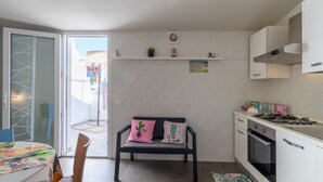 A kitchen with white cabinets, a gas stove, a bench with cushions, a calendar, and a small plant.