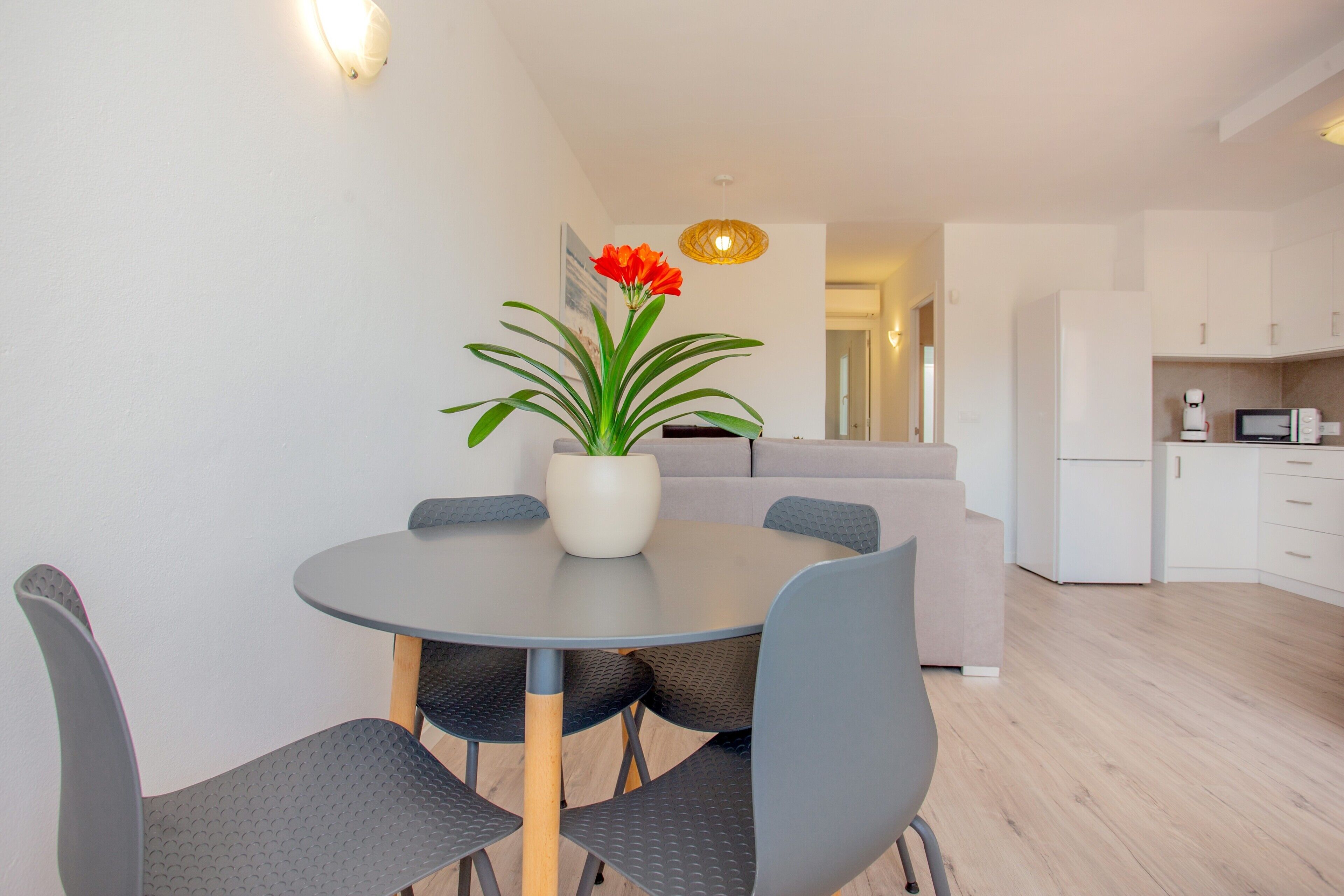 Un espace repas moderne avec une table ronde, des chaises grises, une plante en pot et une cuisine en arrière-plan.