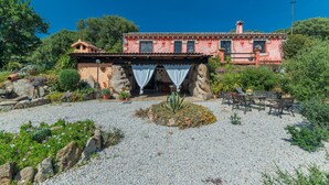 A building with a red facade, a patio with seating, and a garden with various plants. - Villa "Stazzu La Piredda" with Garden & Wi-Fi (Arzachena)