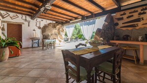 A rustic dining area with wooden beams, a stone wall, and a view of the outdoors. - Villa "Stazzu La Piredda" with Garden & Wi-Fi (Arzachena)