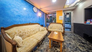 A hotel lobby with a blue wall, a wooden sofa, a wooden table, and a clock. - Laos Otel (Istanbul)