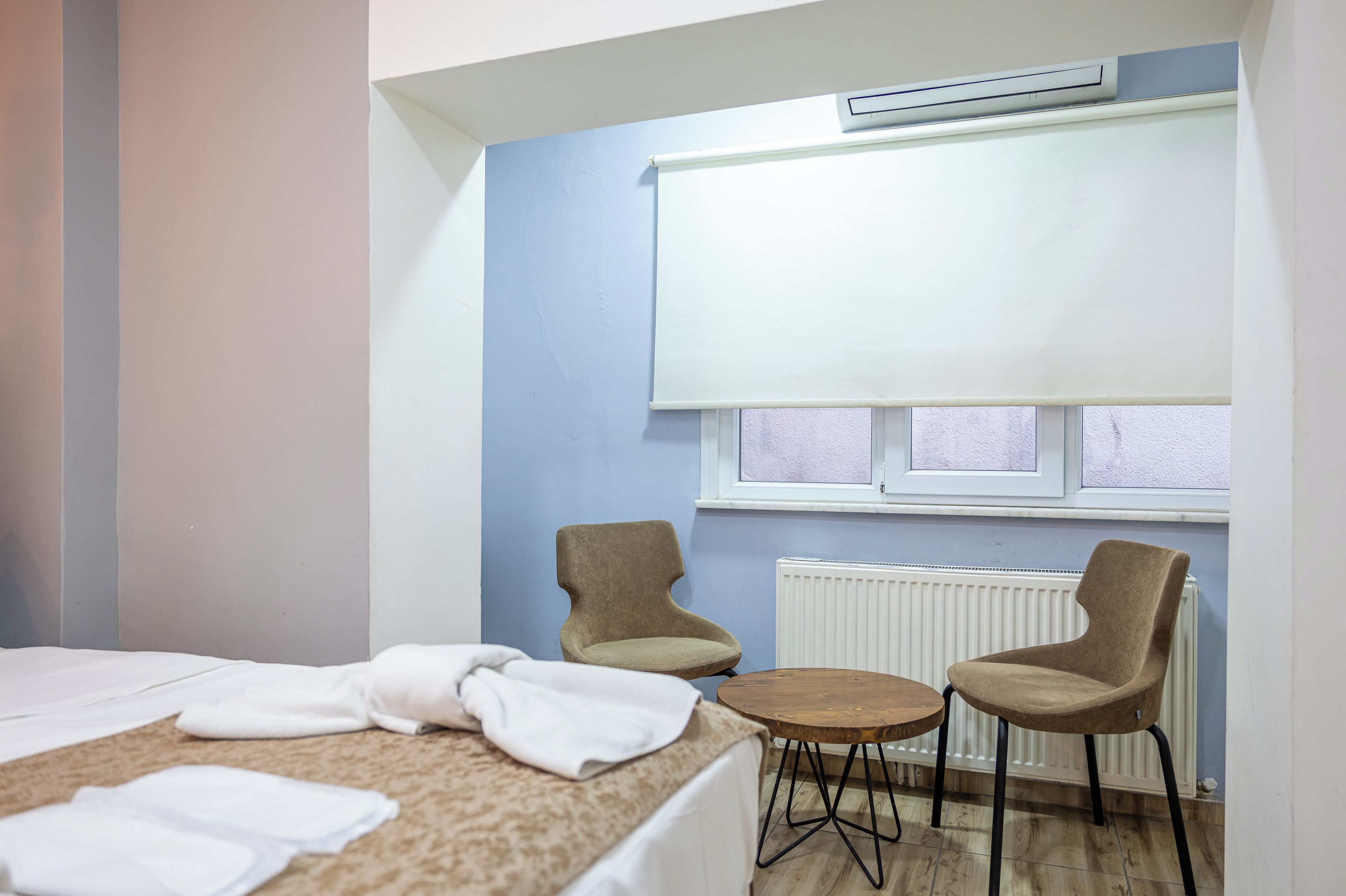 A hotel room with a bed, two chairs, a small table, and a window with blinds.