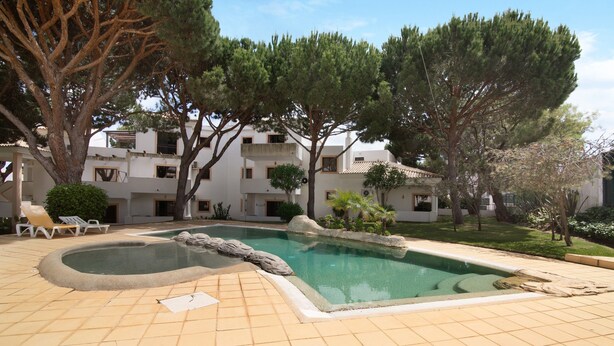 Una piscina amb terrassa enrajolada, gandules i arbres als voltants.