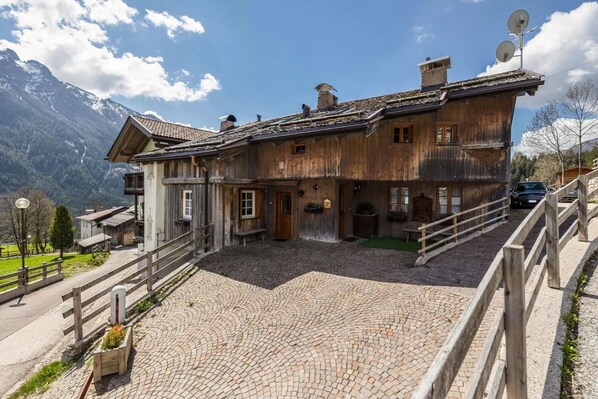 A wooden chalet with a sloped roof, satellite dishes, and a paved courtyard.