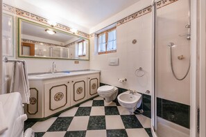 A bathroom with a checkered floor, a toilet, a bidet, a sink, and a shower.