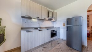 A modern kitchen with light wood cabinets, a stainless steel refrigerator, and a built-in oven.