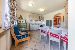 Une cuisine avec des meubles blancs, une table à manger recouverte d’une nappe rouge et une chaise en bois.