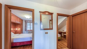A bedroom with a bed, a wooden wardrobe, a mirror, and a desk with a chair.